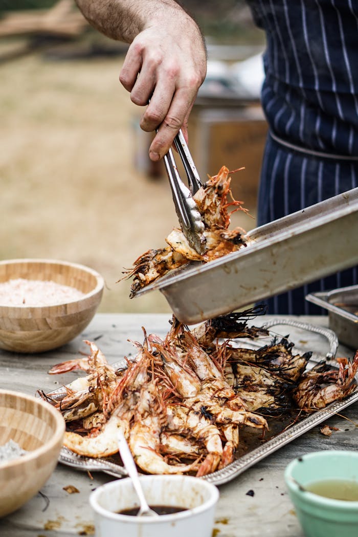 A chef serves a plate of delicious grilled prawns on an outdoor table, ready for a seafood feast.